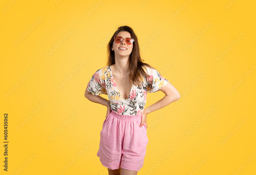 Pretty young caucasian lady wearing trendy summer outfit and colorful sunglasses, posing on yellow studio background Pretty young caucasian lady wearing trendy summer outfit and colorful sunglasses, posing on yellow studio background