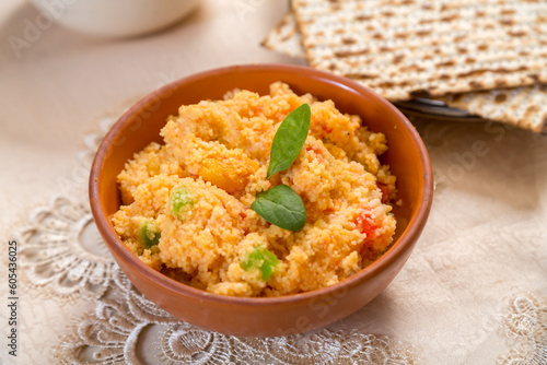 Couscous with dried fruits garnished with herbs in a clay plate on a tablecloth next to a matzah.