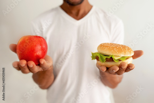 Black Man Holding Burger And Apple Against White Background, Cropped