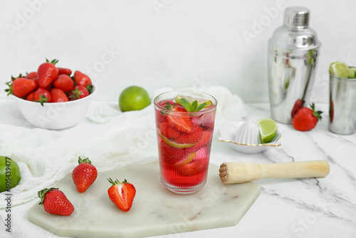 Glass of delicious strawberry mojito on light background