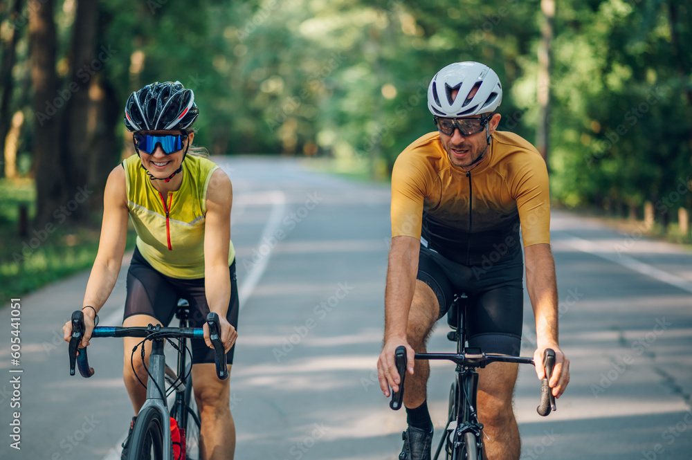 Couple riding bicycles outside of the city and wearing helmets and sunglasses Couple riding bicycles outside of the city and wearing helmets and sunglasses