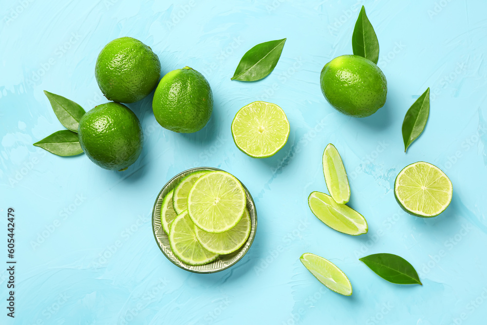 Bowl with slices of fresh lime and leaves on blue background