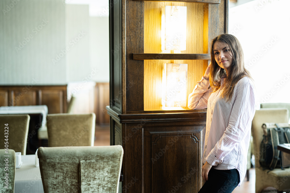 Young beautiful brunette woman stand in restaurant near column with lights. Young beautiful brunette woman stand in restaurant near column with lights.