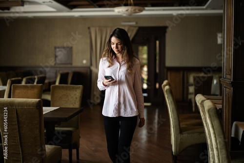 Young beautiful brunette woman walk in restaurant and look at phone.