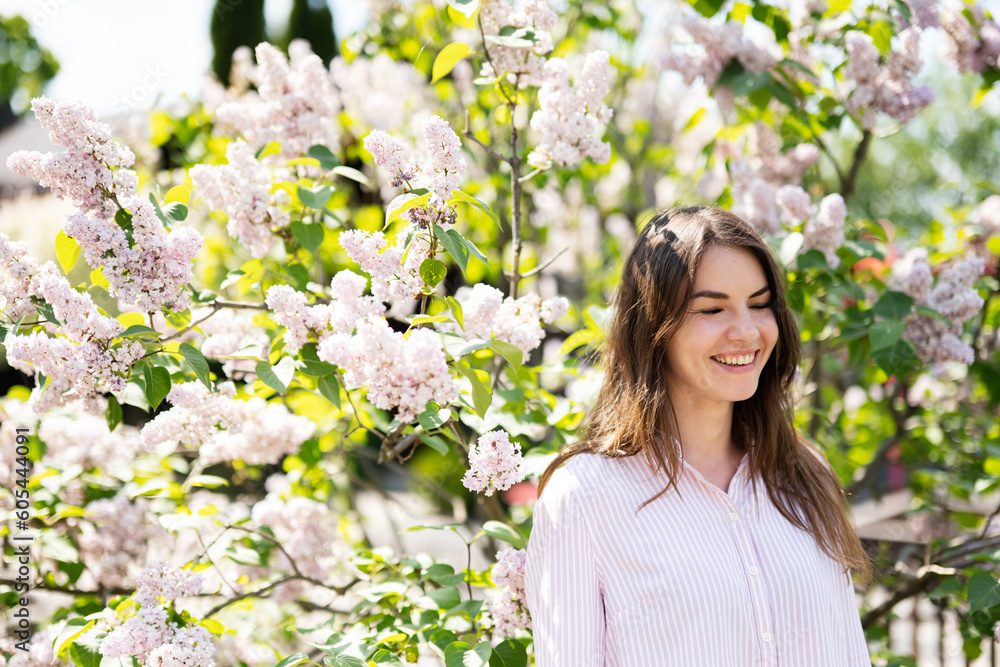 Young smiling brunette woman with closed eyes in shirt near lilac tree. Young smiling brunette woman with closed eyes in shirt near lilac tree.