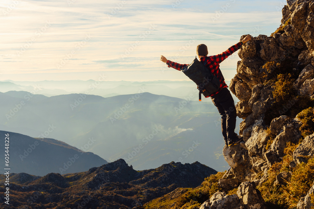 Obraz premium male hiker with backpack climbing a mountain without a rope at sunset. Man contemplating the sunset from the peak of a mountain. sport and adventure.