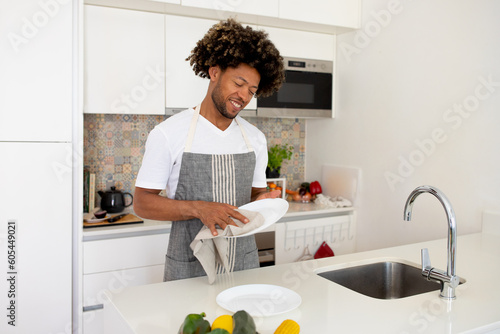 Fotografie African Guy Doing Dishes Drying Plate With Towel In Kitchen