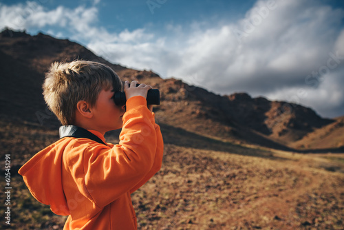 Portrait of boy tourist looking in binoculars in mountains