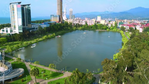 Drone flies in park with lake against backdrop of skyscrapers and mountains on May 6. park facilities for children, as well as children's playground by sea on sunny day. See city of Batumi in Georgia photo