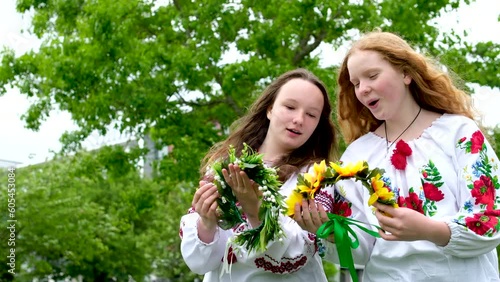 two beautiful Ukrainian girls weave wreaths embroidered shirts greenery nature sit near house Ukrainian entertainment at parties rest communication sing songs national rites laugh smile talk photo
