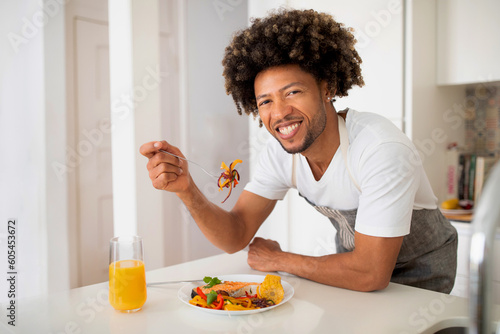 African Man Enjoying Meal Eating Fish And Vegetables In Kitchen