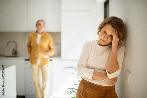 Upset elderly caucasian couple standing in kitchen after argue, selective focus on aged crying woman