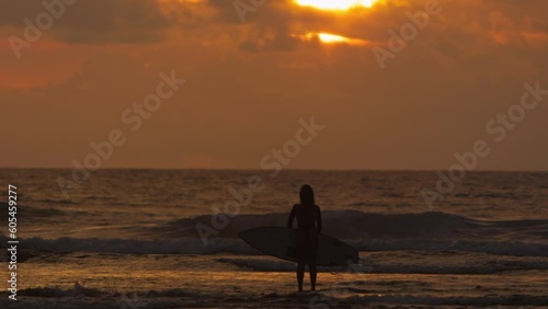 Silhouette of bodyboarder person by ocean waves at golden sunset, cinematic. Person bodyboarder with bodyboard on ocean. Concept of contemplation and enjoyment of seascape in rays of golden sunset sun photo