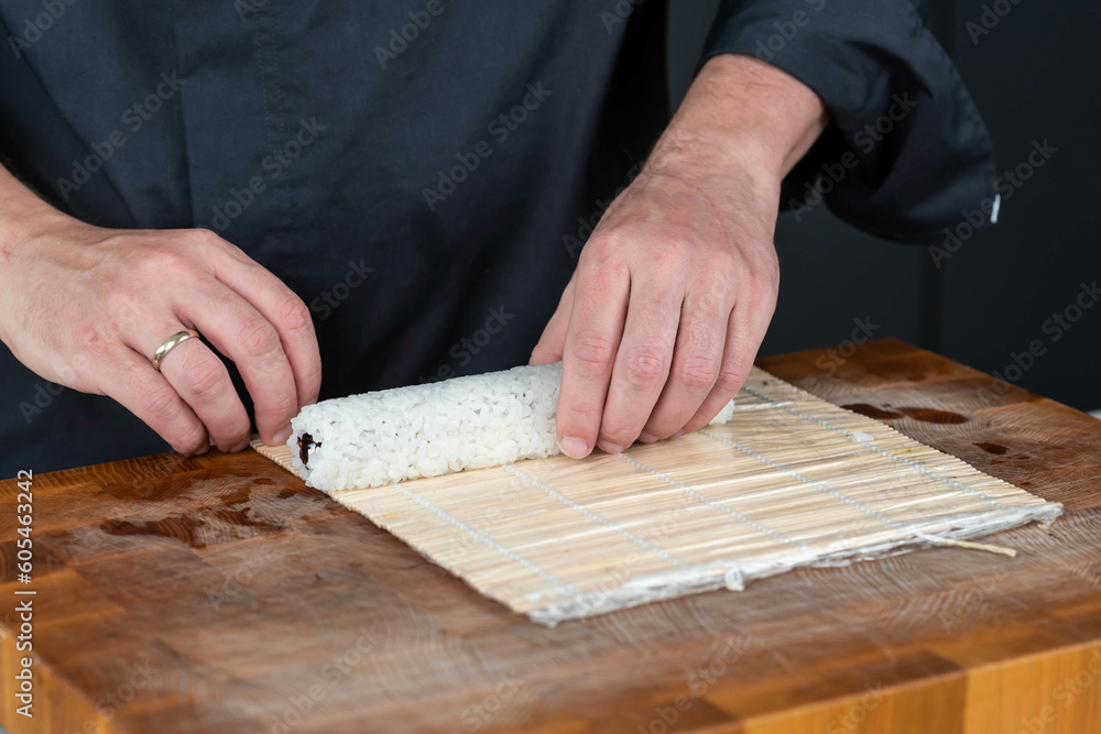 Close up of sushi chef hands preparing japanese food. Man cooking sushi with red caviar, avocado and cheese at restaurant. Traditional asian seafood rolls on cutting board. Close up of sushi chef hands preparing japanese food. Man cooking sushi with red caviar, avocado and cheese at restaurant. Traditional asian seafood rolls on cutting board.