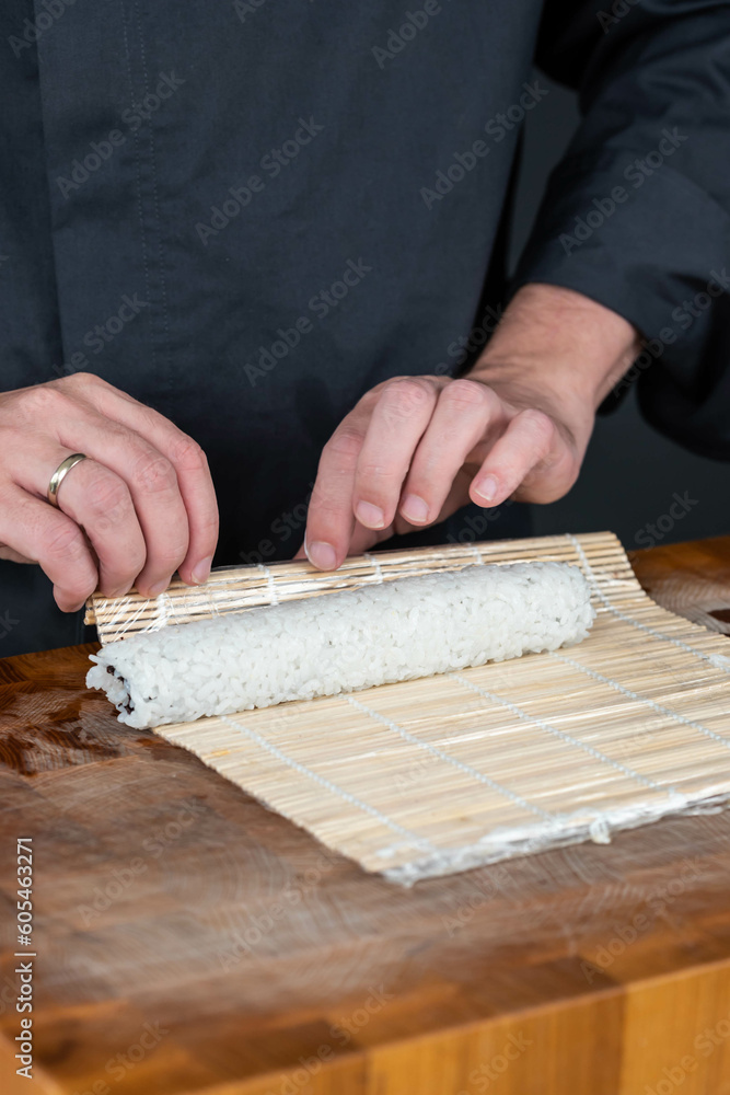 Close up of sushi chef hands preparing japanese food. Man cooking sushi with red caviar, avocado and cheese at restaurant. Traditional asian seafood rolls on cutting board.