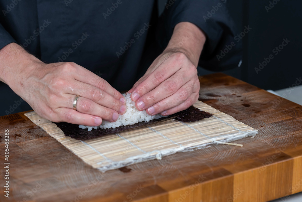 Close up of sushi chef hands preparing japanese food. Man cooking and making rice for sushi at restaurant. Traditional asian seafood rolls on cutting board. Close up of sushi chef hands preparing japanese food. Man cooking and making rice for sushi at restaurant. Traditional asian seafood rolls on cutting board.
