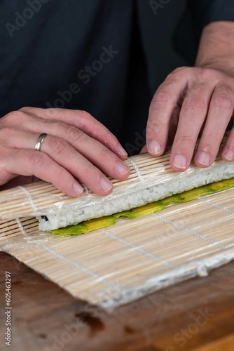 Close up of sushi chef hands preparing japanese food. Man cooking sushi with red caviar, avocado and cheese at restaurant. Traditional asian seafood rolls on cutting board.