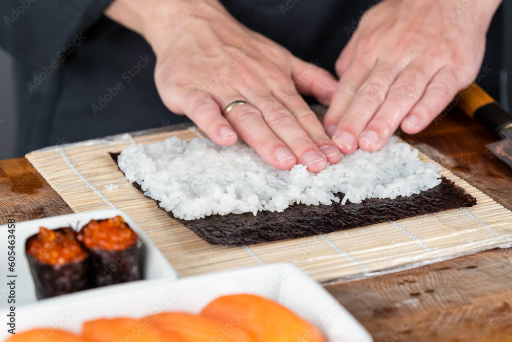 Close up of sushi chef hands preparing japanese food. Man cooking sushi with red caviar and salmon at restaurant. Traditional asian seafood rolls on cutting board. Close up of sushi chef hands preparing japanese food. Man cooking sushi with red caviar and salmon at restaurant. Traditional asian seafood rolls on cutting board.