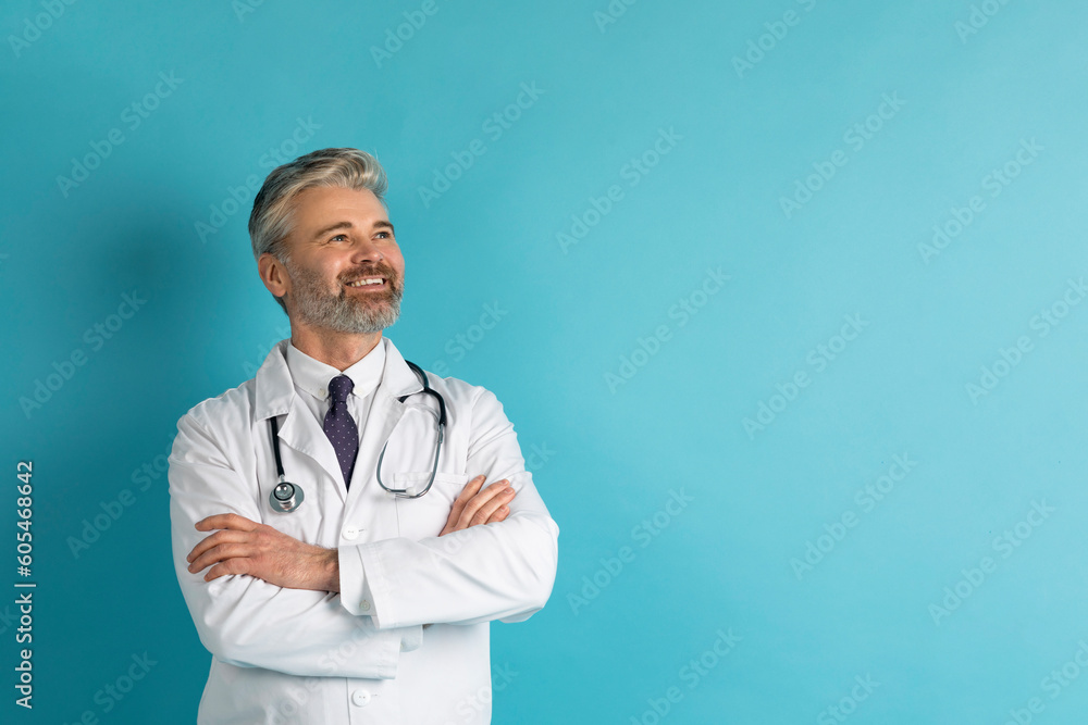 Handsome mature european doctor posing on blue, copy space Handsome mature european doctor posing on blue, copy space
