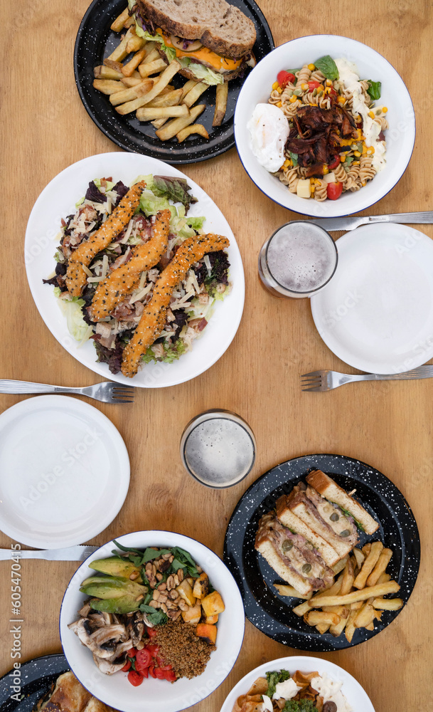 Food. Eating at the restaurant. Top view of variety of gourmet dishes, tableware and glasses of beer, on the wooden table. Food. Eating at the restaurant. Top view of variety of gourmet dishes, tableware and glasses of beer, on the wooden table.