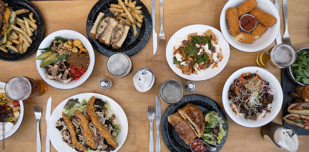 Food banner. Top view of variety of gourmet dishes, tableware and glasses of beer, on the wooden table. Food banner. Top view of variety of gourmet dishes, tableware and glasses of beer, on the wooden table.