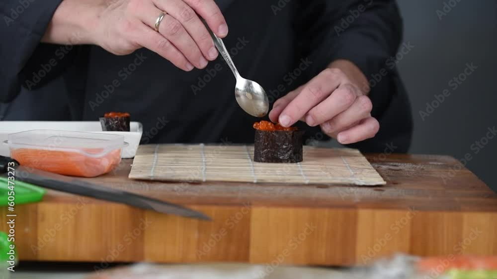Close up of sushi chef hands preparing japanese food. Man cooking sushi with red caviar and salmon at restaurant. Traditional asian seafood rolls on cutting board. Close up of sushi chef hands preparing japanese food. Man cooking sushi with red caviar and salmon at restaurant. Traditional asian seafood rolls on cutting board.