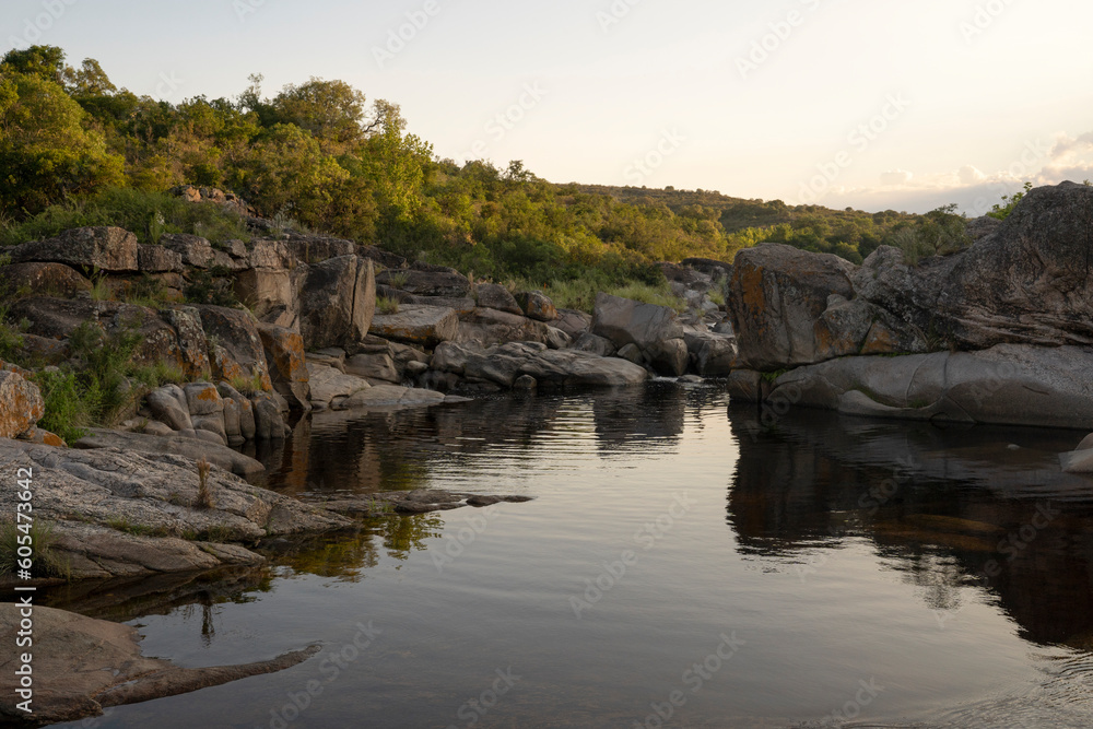 View of the river across the rocky hills at sunset. The sky reflection in the water surface.