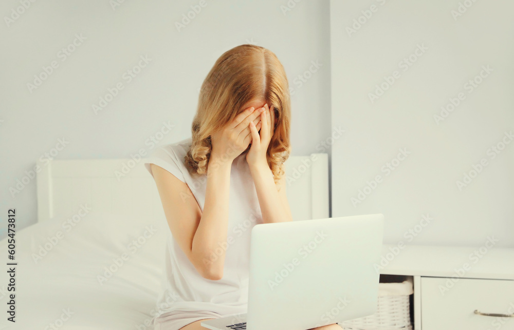 Portrait of sad upset crying young woman working with laptop on the bed in white room at home Portrait of sad upset crying young woman working with laptop on the bed in white room at home