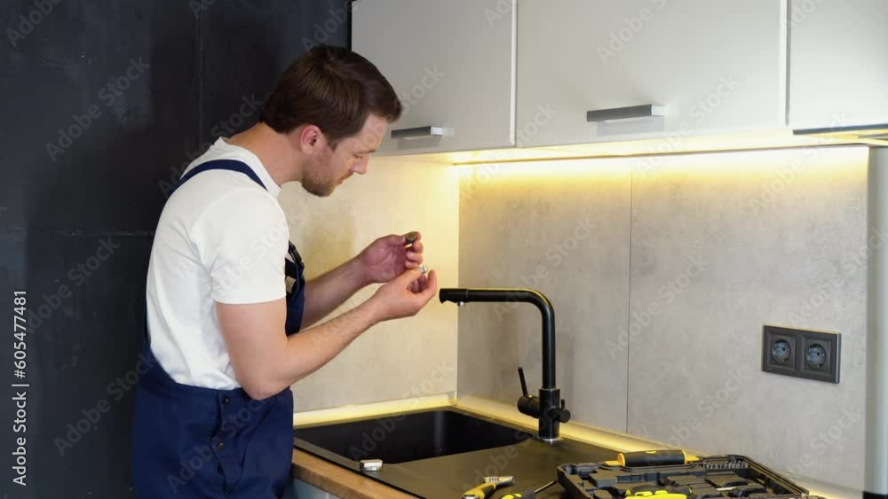 Repair of the faucet in the kitchen near the sink. A plumber in the kitchen installs a new water tap Repair of the faucet in the kitchen near the sink. A plumber in the kitchen installs a new water tap