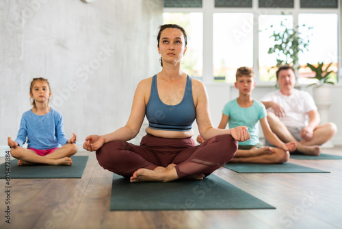 Adult woman with her husband and children doing yoga in fitness class