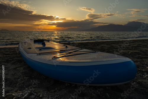 An inflatable surfboard lies on the seashore against the background of the sunset