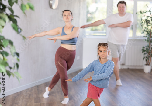 Cute little girl practicing dance movements together with her parents and brother during training session