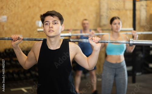Concentrated athletic guy taking part in intense group training in modern gym, performing exercises with barbell. Fitness and bodybuilding concept..