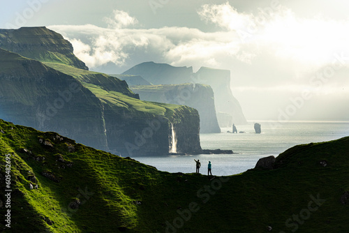 Silhouette of hikers admiring cliffs standing on top of mountain ridge above the ocean, Kalsoy island, Faroe Islands, Denmark, Europe photo