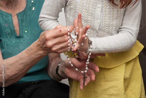 abuela y nieta rezando sujetando un rosario photo