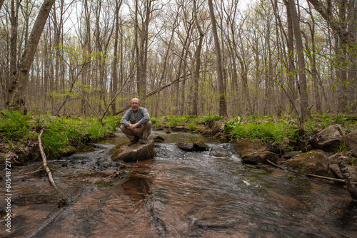 A senior man crouches on stepping stone hiking across a stream © Mary Salen