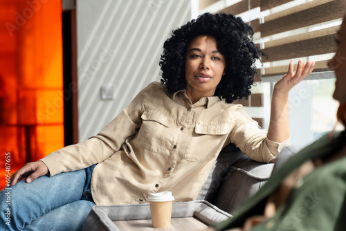 Φωτογραφία Relaxed young African American woman sitting on sofa, talking with colleague whi