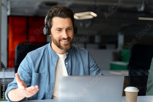 Quadro su tela Handsome smiling latin call center operator wearing headphones answering call, communication online sitting in modern office