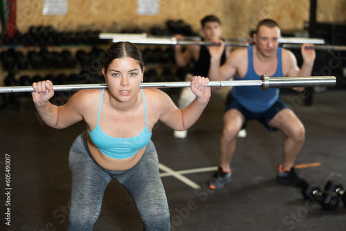 Motivated CrossFit female athlete lifting heavy body bar or barbell during group training in gym. Functional training concept.