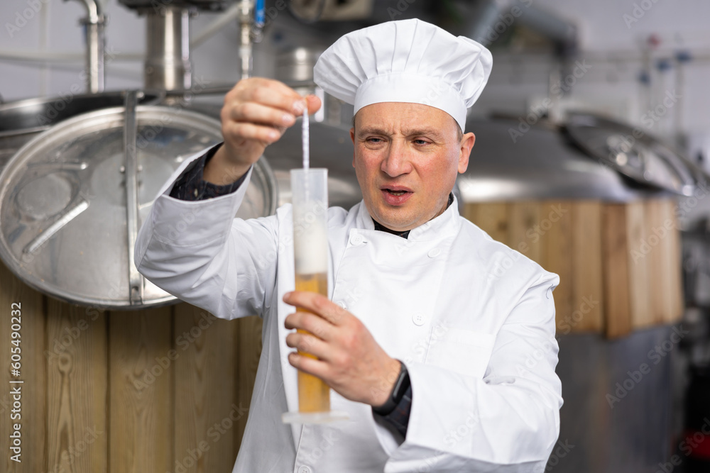 Frustrated man brewmaster in white coat measuring beer sample with alcoholometer.