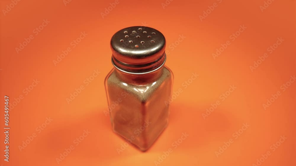 glass pepper shaker with metal cap turns on orange closeup glass pepper shaker with metal cap turns on orange closeup