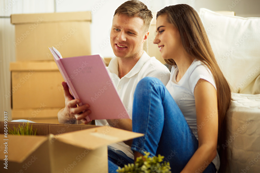 Young couple holding album while sitting on floor in new house Young couple holding album while sitting on floor in new house