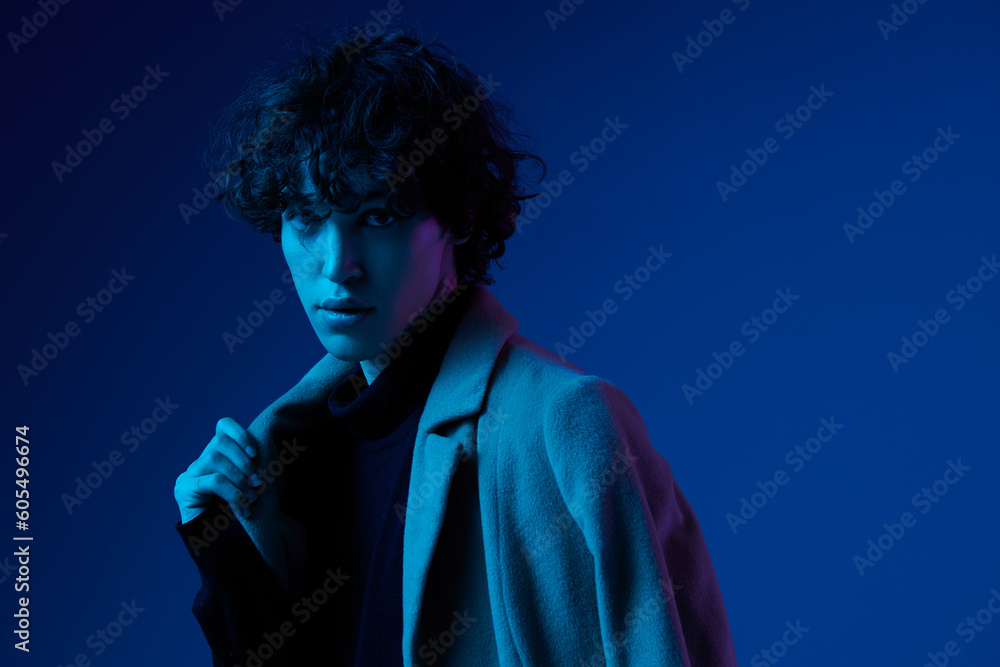 Man fashion in jacket poses against dark blue background, neon light, style and trends, mixed light, men's fashion, copy place