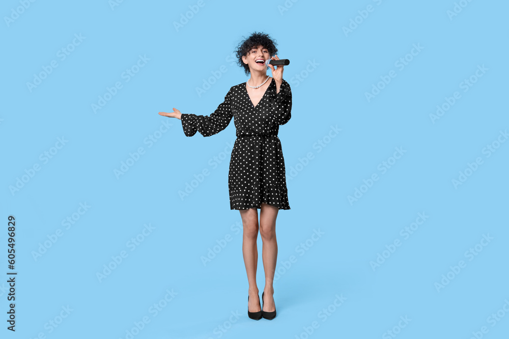 Beautiful young woman with microphone singing on light blue background Beautiful young woman with microphone singing on light blue background