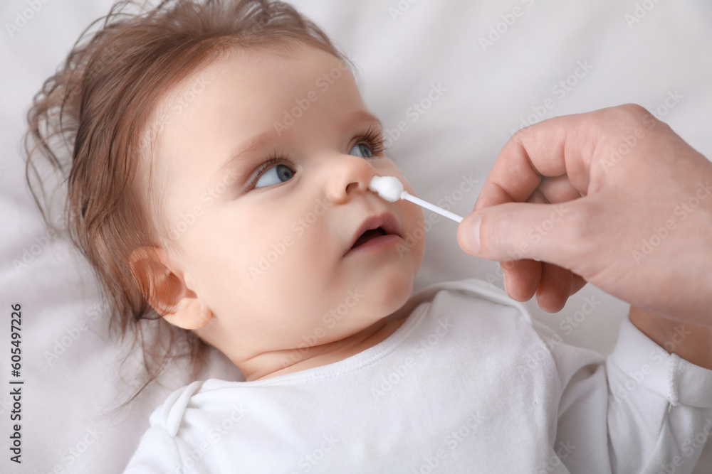 Father cleaning nose of his baby with cotton bud on bed, closeup Father cleaning nose of his baby with cotton bud on bed, closeup