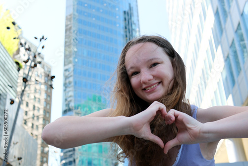 Canvas Print beautiful girl shows heart with hands against backdrop of skyscrapers and big ci