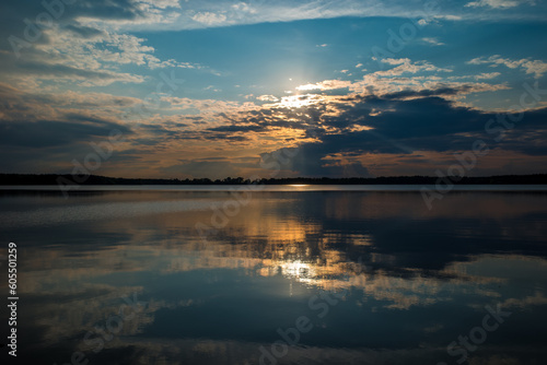 Sunset behind clouds over the lake, sun rays reflecting in the water. High quality photo