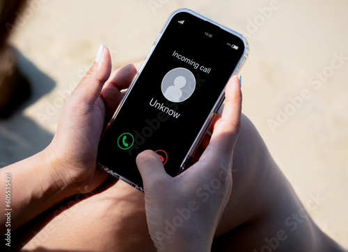 Incoming call with unknown caller, malicious phone calls concept. Unknown number displayed showing on smart mobile phone in woman hand on leave day at the beach. Spam and robocalls, scam call alert. photo