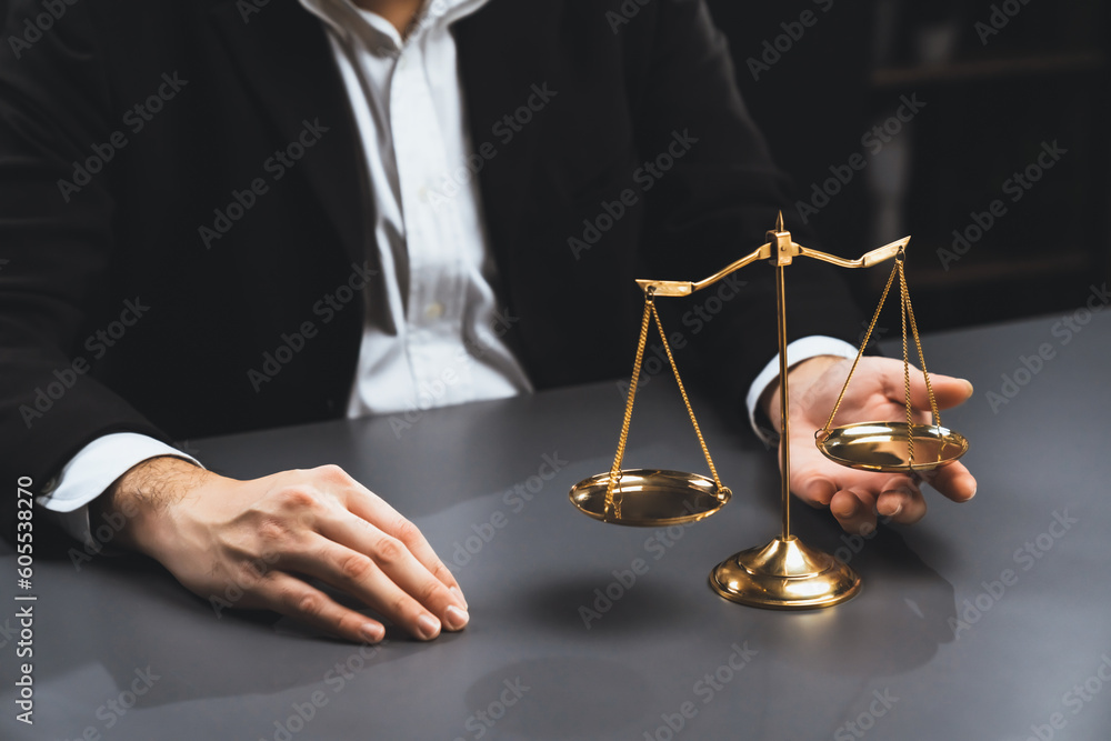 Lawyer in a black suit sits attentively on his office desk with a golden scale balance, symbol of legal justice and integrity, balanced and ethical decision making in the court of law. equility - obrazy, fototapety, plakaty 