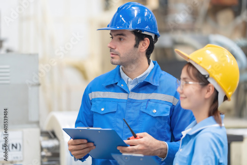 Half body shot of a male American engineer and an Asian female manager nearby. looking at the destination together Wear uniforms and helmets. in the plastic industry surrounded by machines